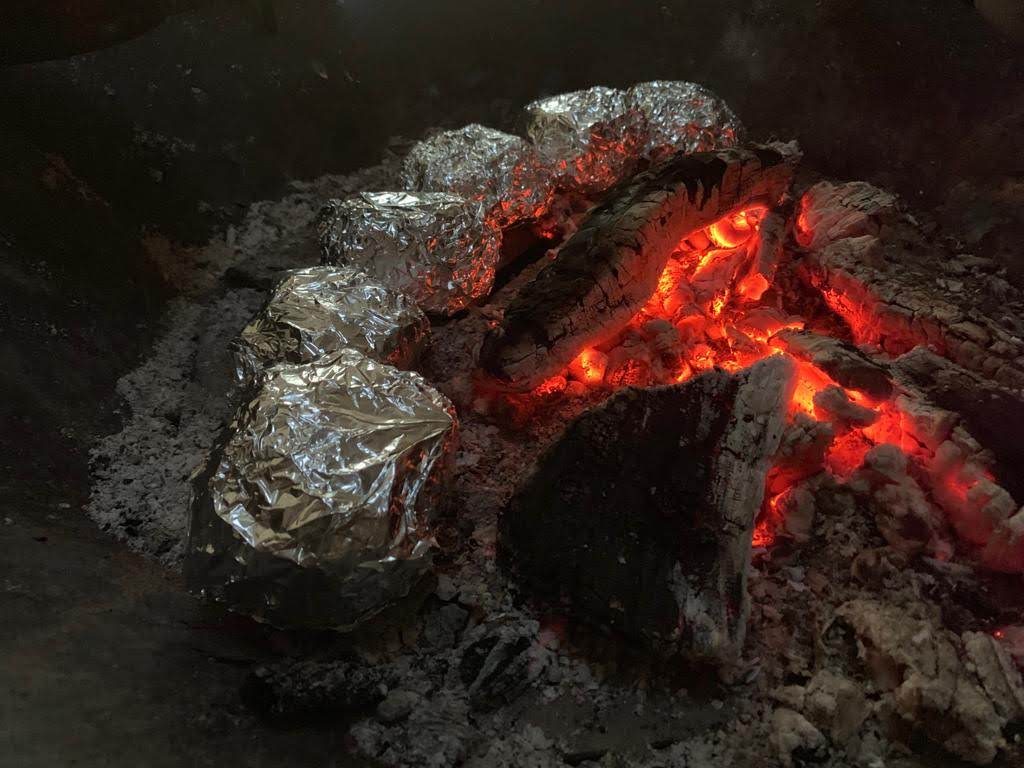 Folioon käärittyjä sämpylöitä hiilloksen ympärillä nuotiossa.